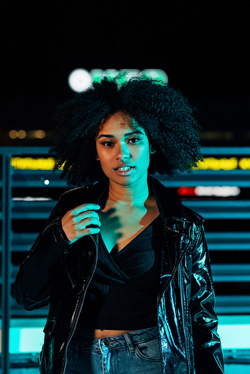 Young girl in leather jacket posing at night under neon lights