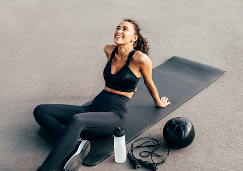 Happy woman sitting on a mat and looking up after evening work out