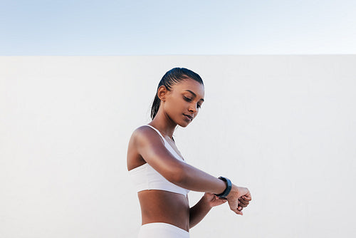 Side view of slim female in white sports bra looking on a smartwatch. Young sportswoman checking heart rate.