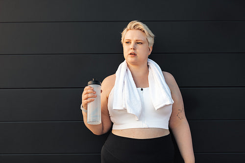 Portrait of a tired curvy woman standing at wall with a towel around a neck