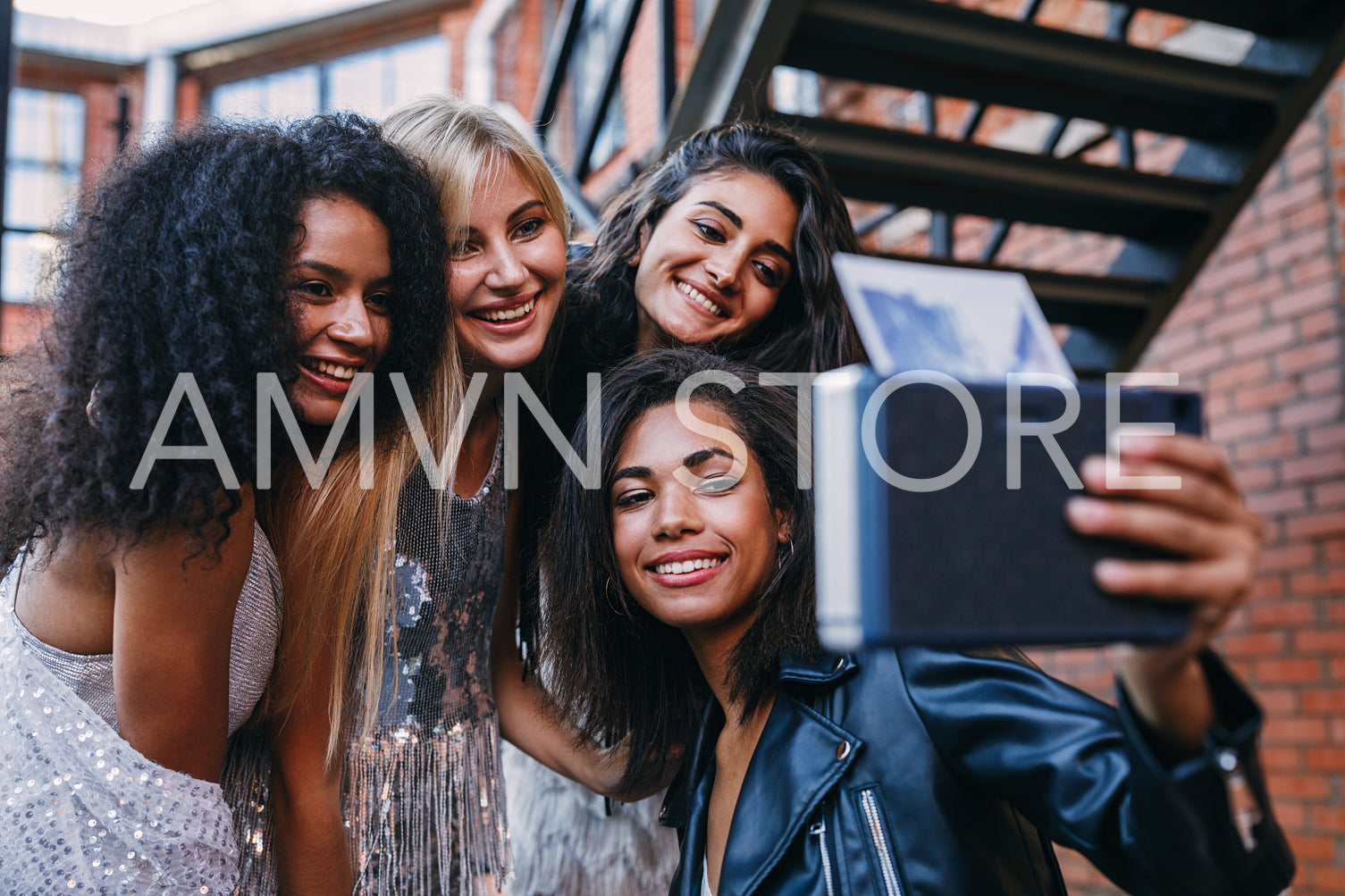 Four happy female friends taking an instant photo. Group of women taking selfie on instant camera outdoors.	