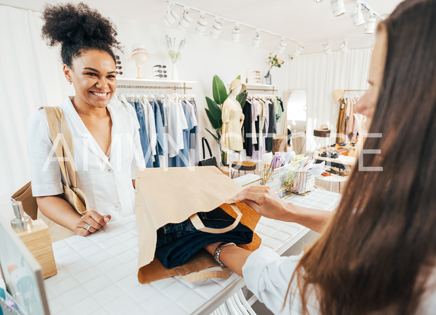 Unrecognizable clothing store owner packing the clothes in a paper bag. Smiling buyer looking at saleswoman while she packing purchase.