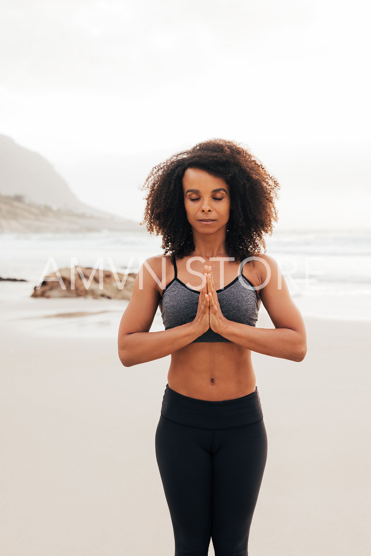 Woman meditating with eyes closed while practicing yoga at sunset on a beach