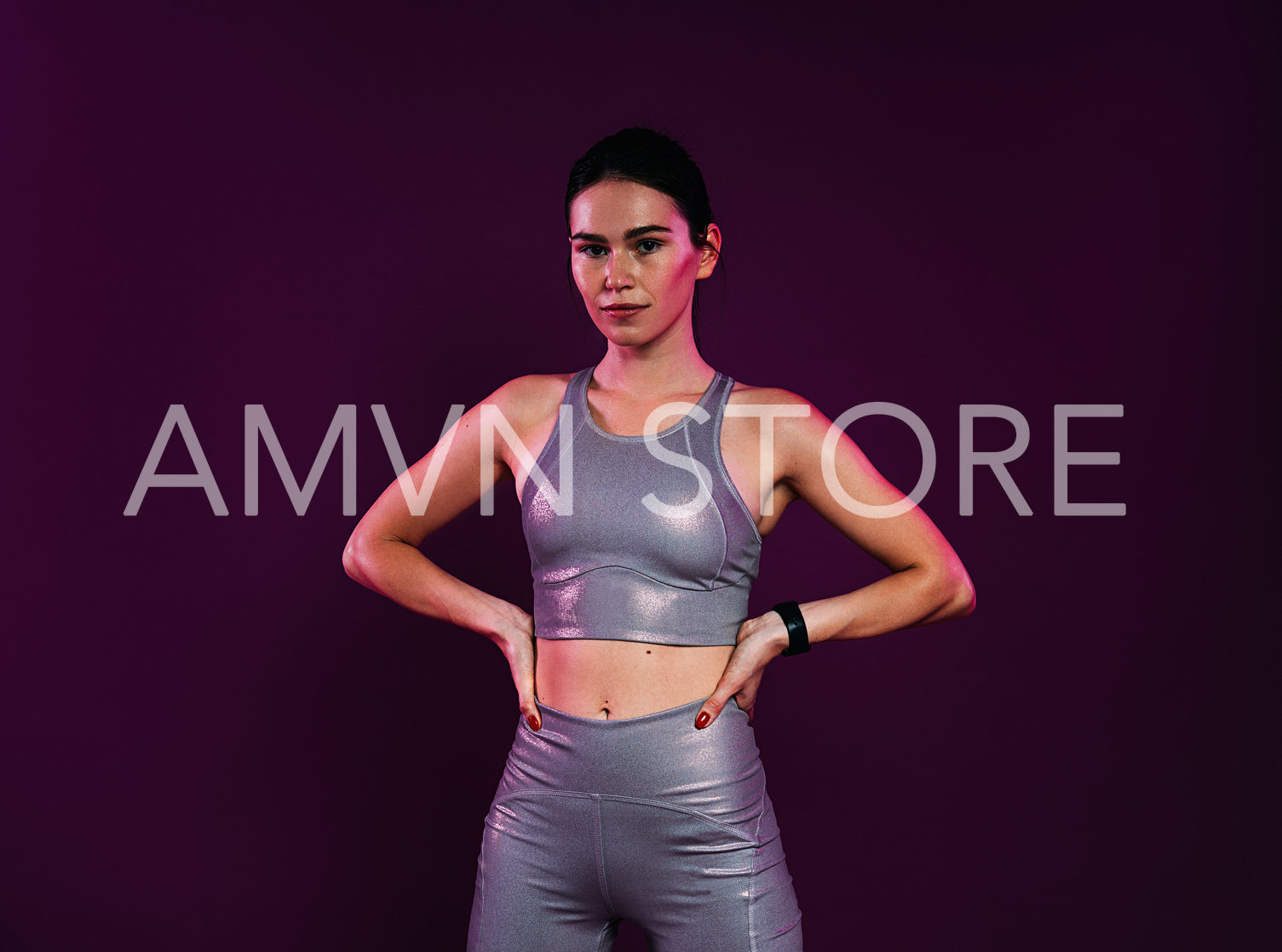 Smiling woman athlete in silver sportswear with hands on hips standing at magenta backdrop