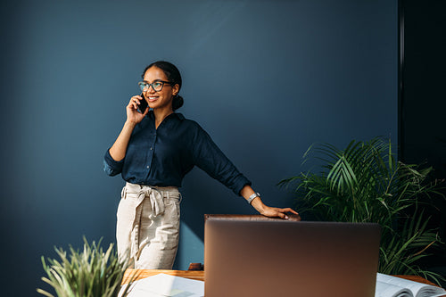 Happy entrepreneur leaning to a chair and looking away while talking on mobile phone