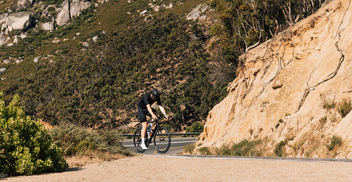 Young male cyclist practicing on an empty road in wild terrain