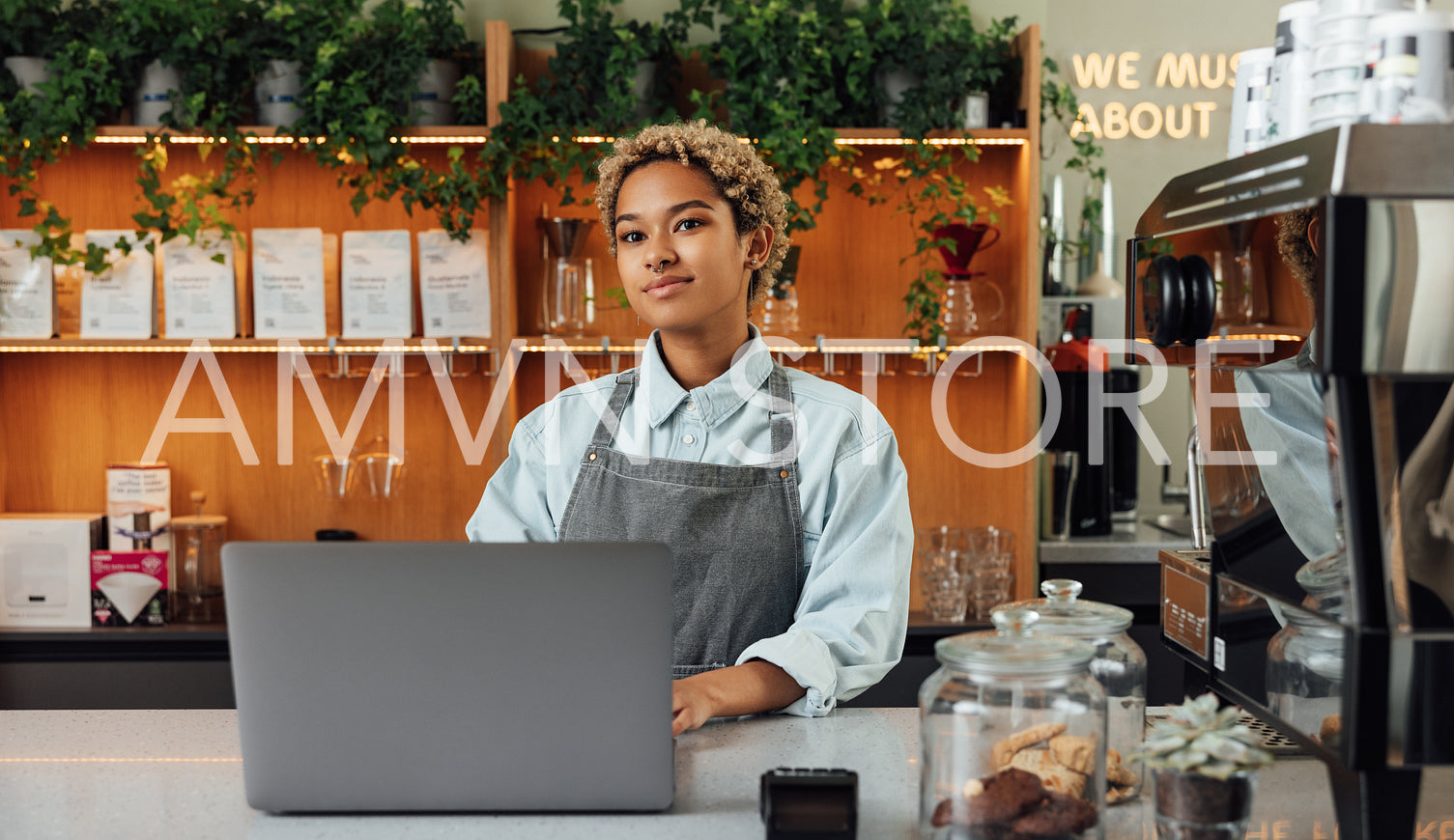 Young female coffee shop owner at counter with a laptop. Woman barista in an apron working in a coffee shop.