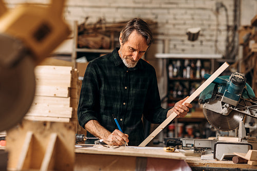 Senior carpenter holding a plank and drawing on paper after measurements