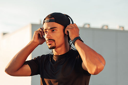 Male athlete in cap wearing wireless headphones during outdoor workout