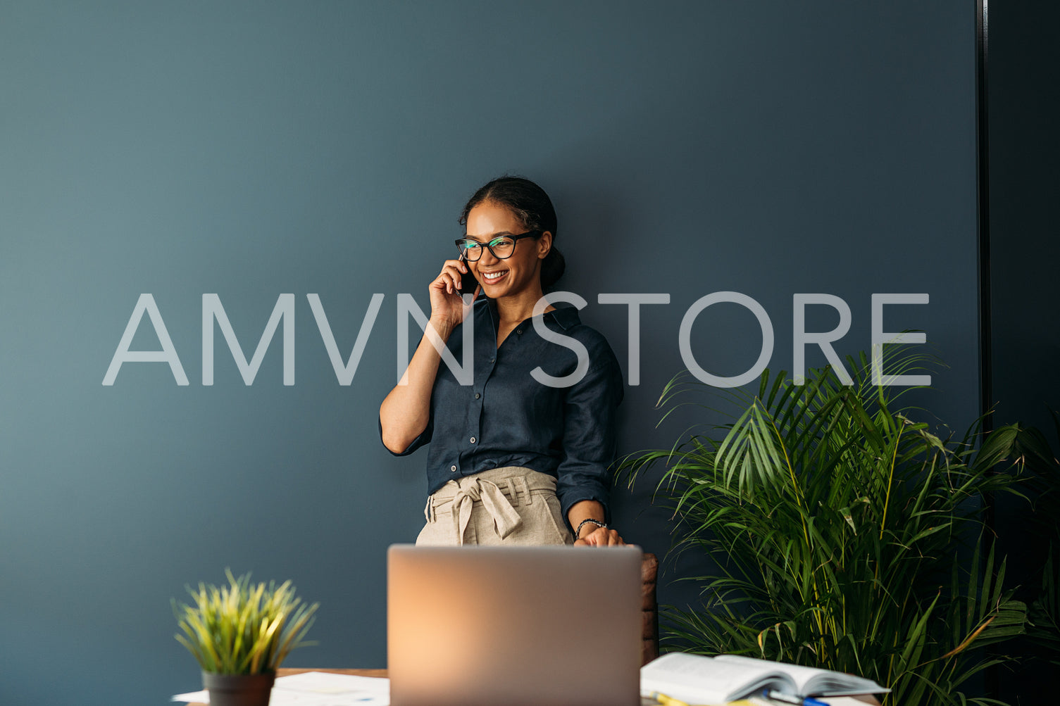 Cheerful businesswoman in formal wear leaning blue wall in home office