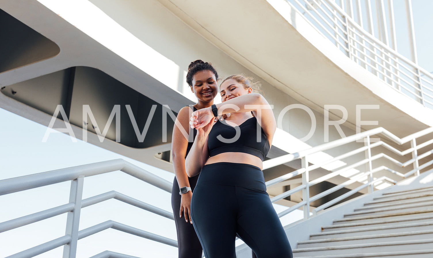 Two smiling female athletes looking at the smartwatch. Plus size female showing her fitness friend result of a workout on a smartwatch.