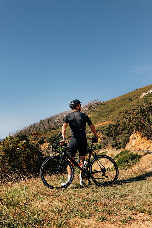 Rear view of a male road bike rider leaning his bicycle while standing in wild terrain