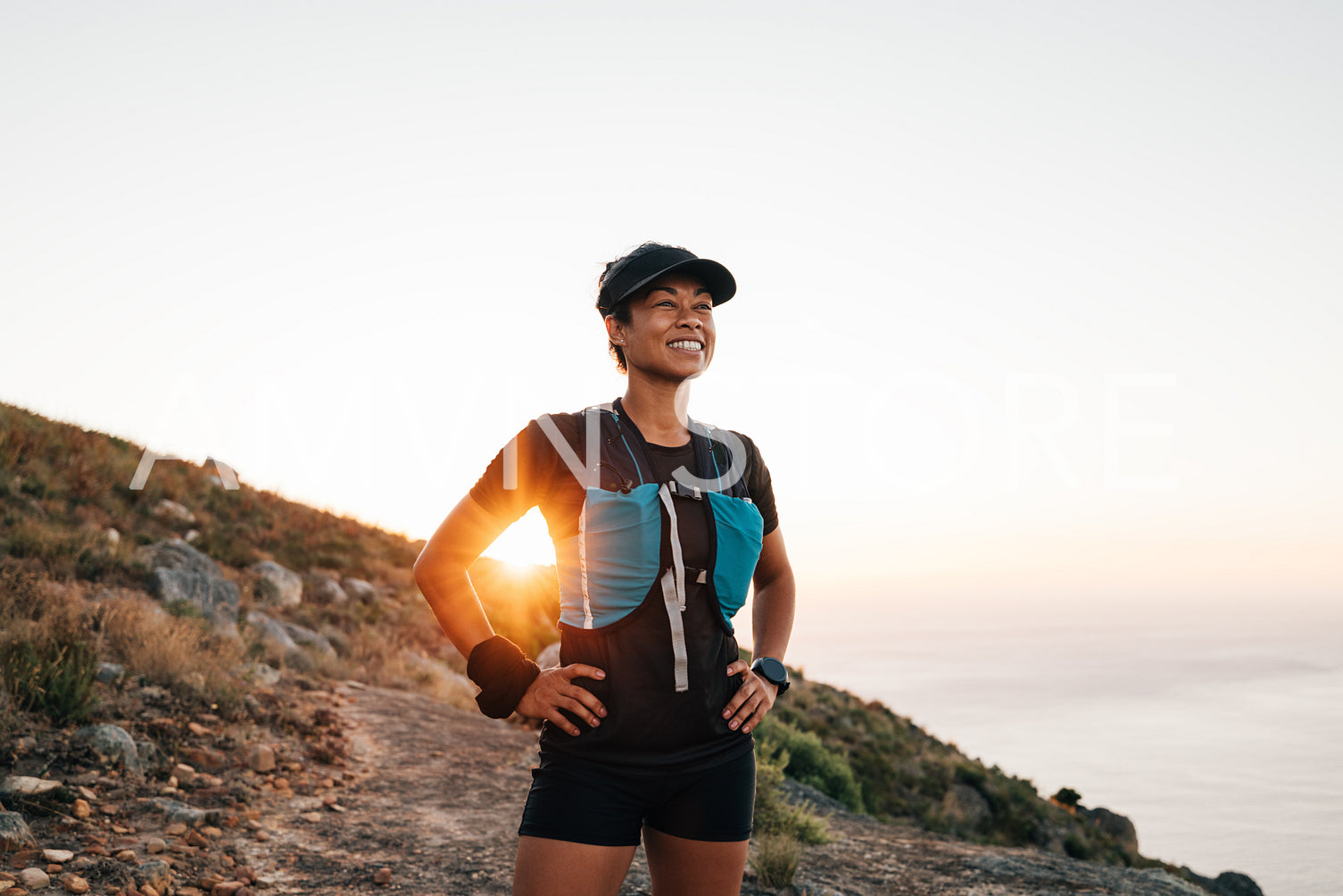 Portrait of sporty woman with cap relaxing at sunset. Female taking break on trail run.