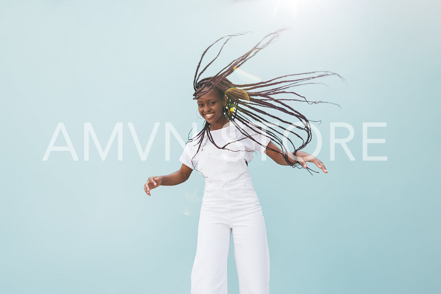 Happy woman in casuals making her long braided hair fly in air at wall