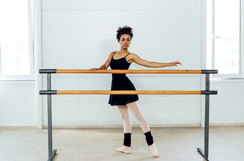 Female ballet dancer with curly hair holding a barre preparing for a ballet class in a studio