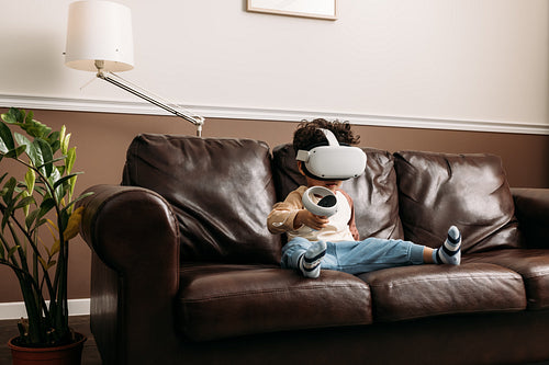 Little boy playing virtual reality game while sitting on sofa in