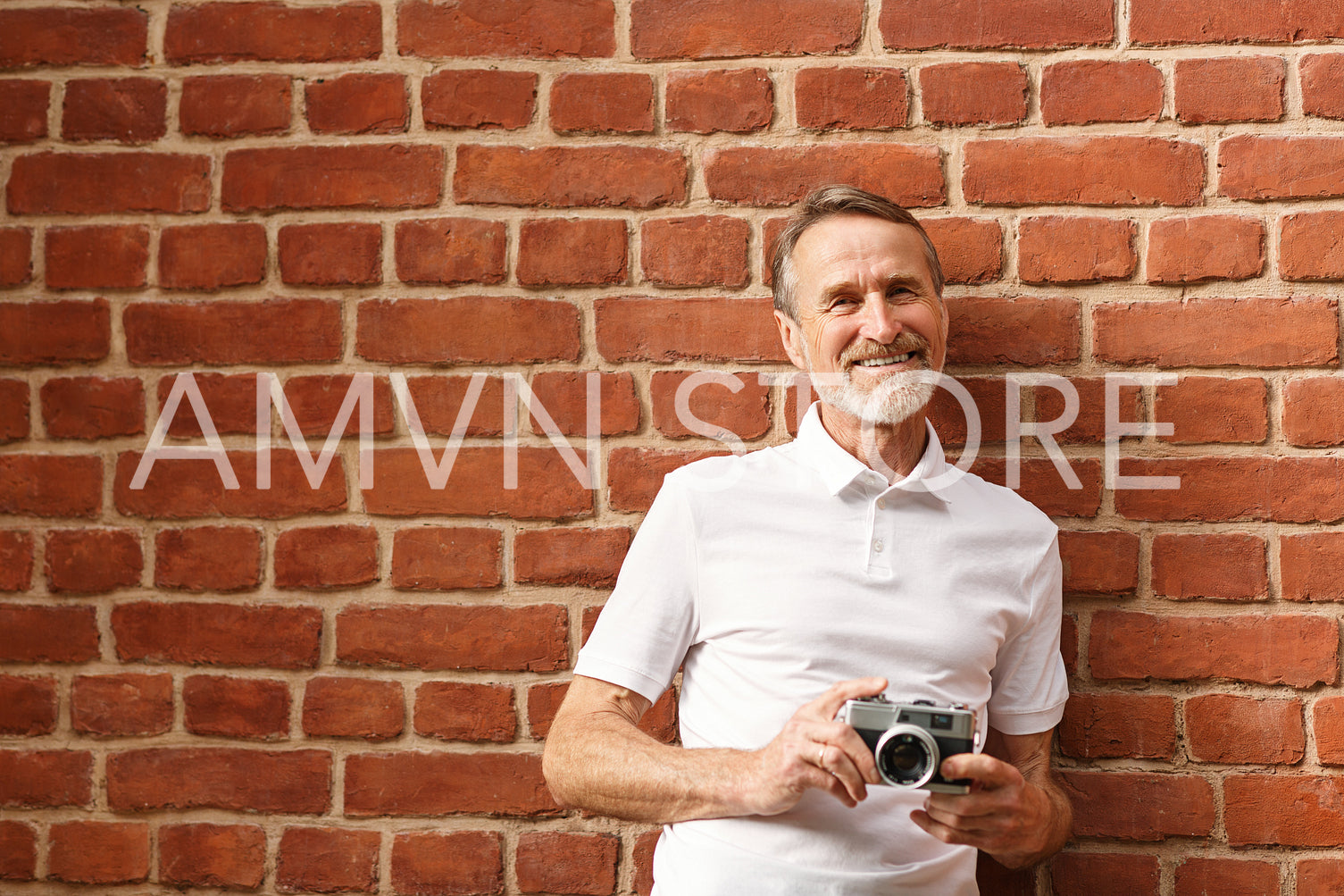 Smiling mature man looking at camera. Tourist with camera standing at brick wall.	