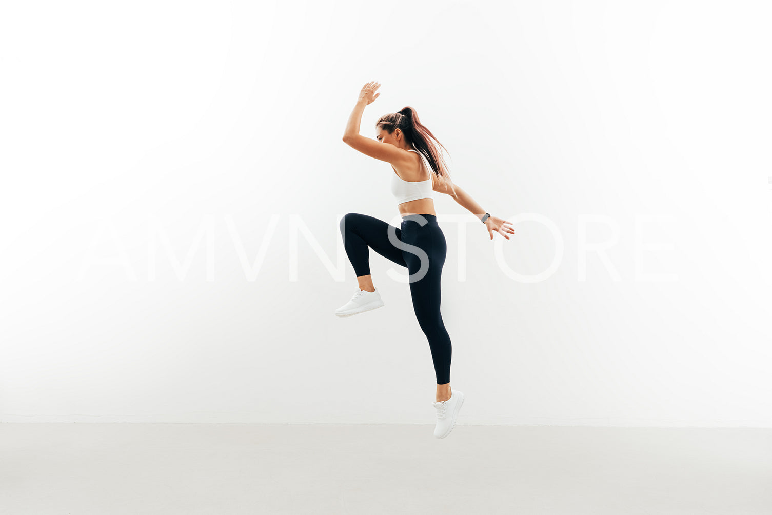 Sportswoman jumping up indoors. Female athlete warming up against a white wall.