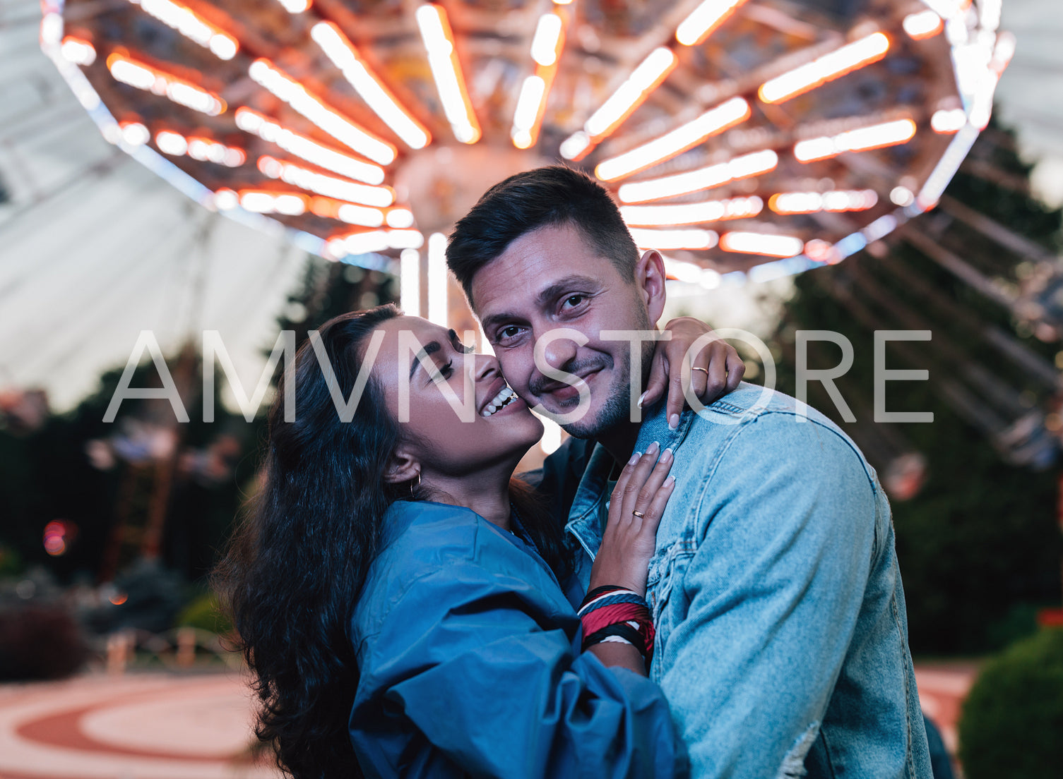 Young couple embracing and having fun in amusement park against carousel