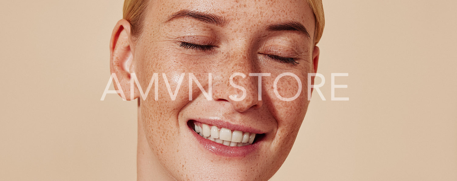 Close up highly detailed studio shot of a young female with freckles. Portrait of a smiling woman with blond hair and smooth skin against a beige background.