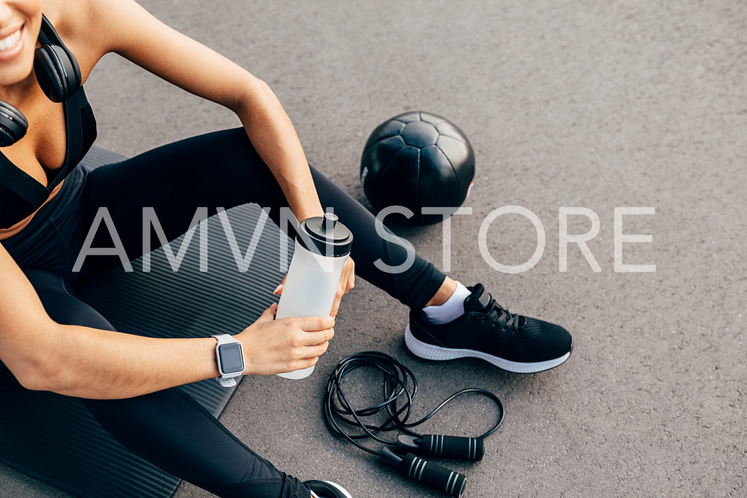 Cropped shot of unrecognizable sport woman sitting on a mat outdoors and holding bottle	