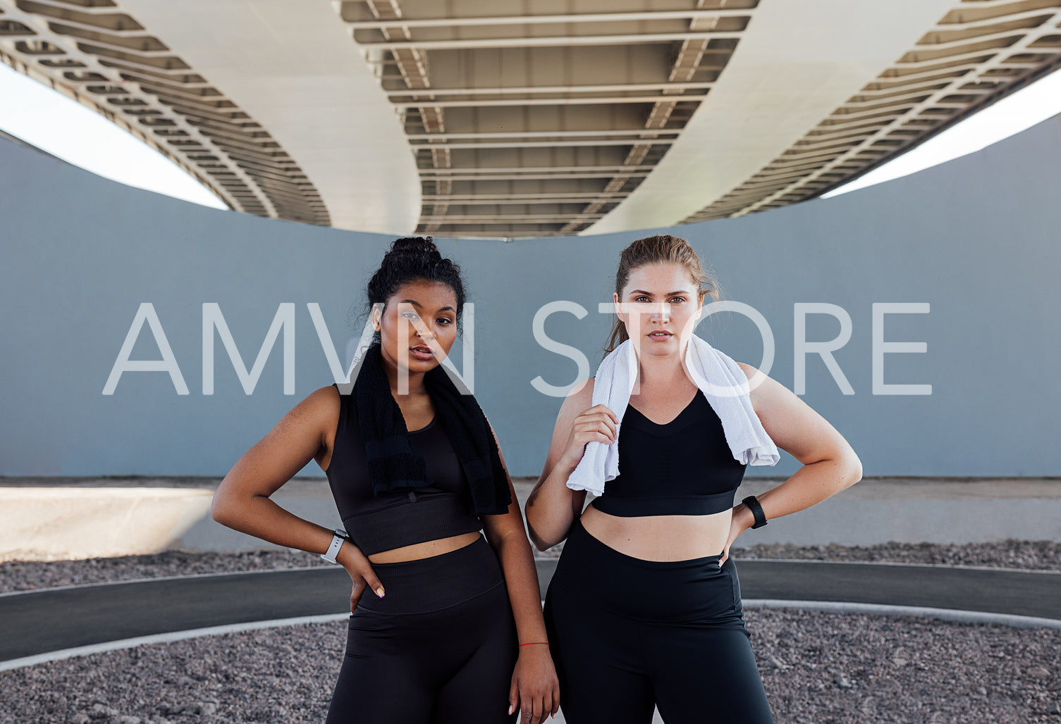 Portrait of two women in black fitness wear with towels on their necks. Young sportswomen are relaxing outdoors.