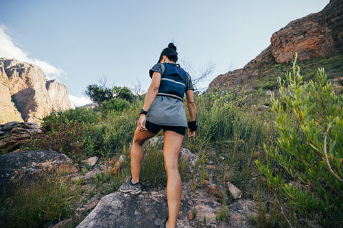 Rear view of woman walking up on mountain trail. Female hiker in sportswear doing hike in wild terrain.