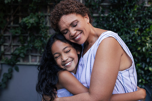 Granny and kid hugging. Happy grandma and granddaughter embracing with closed eyes at backyard.