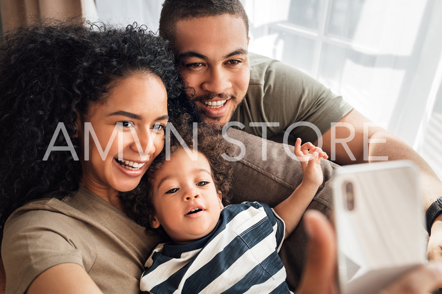 Family posed for a selfie together in living room. Father, mother, and their little son looking at a smartphone camera.	