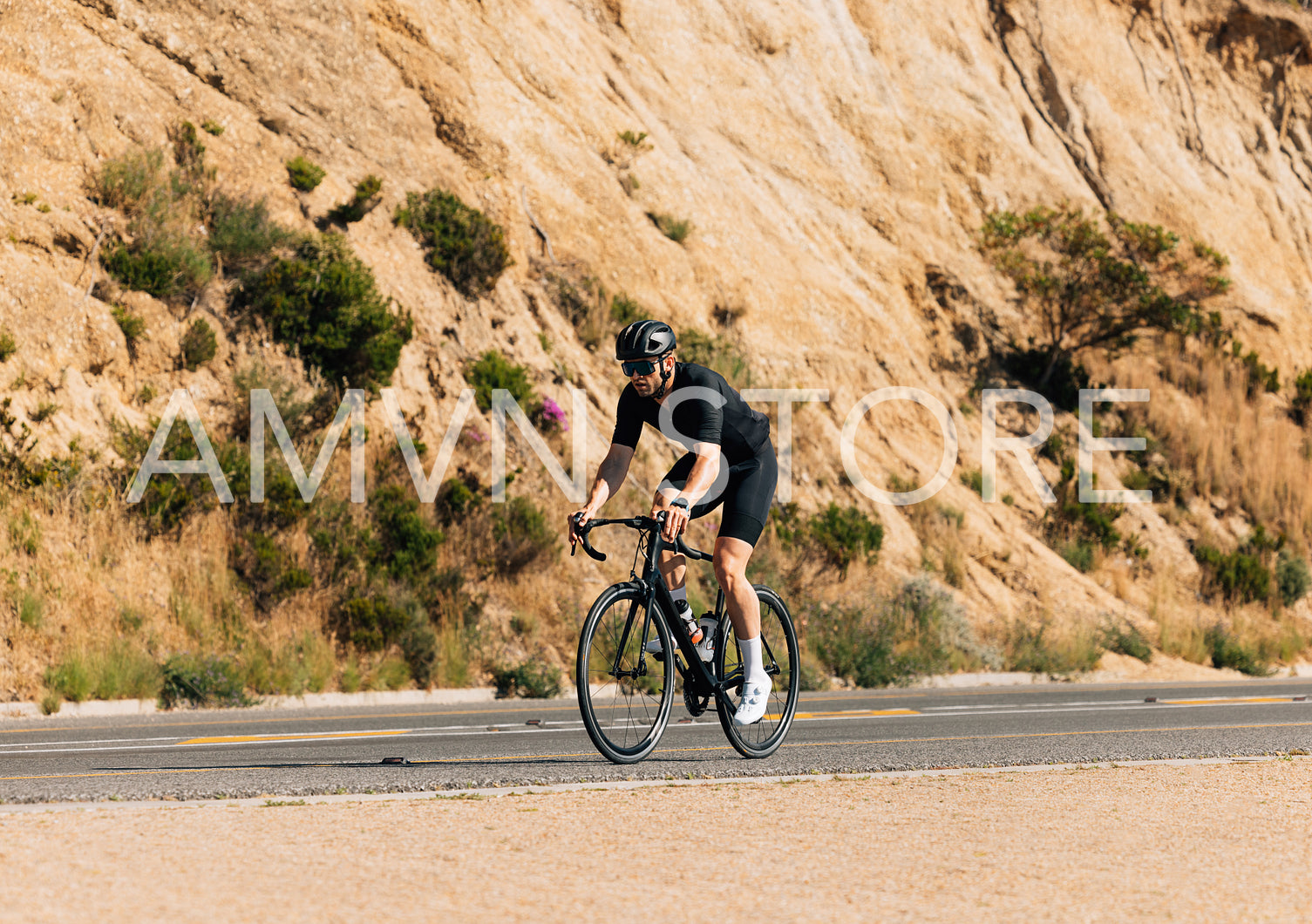 Young male in black sportswear riding a bicycle on an empty road a mountain