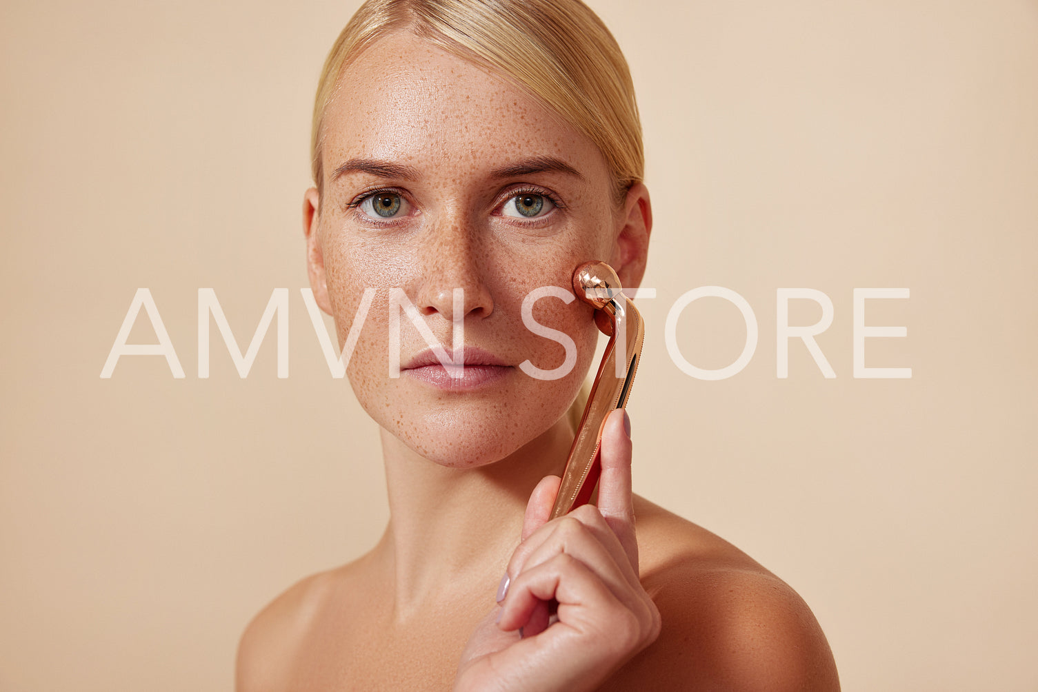 Young woman with smooth skin using a facial roller. Blond female doing skincare routine.