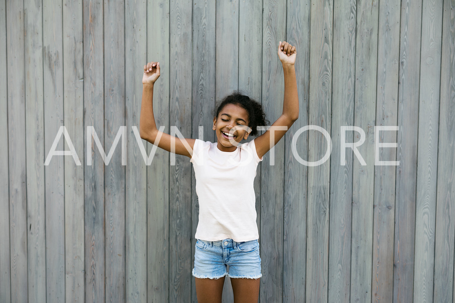 Happy girl standing at wall with raised hands	