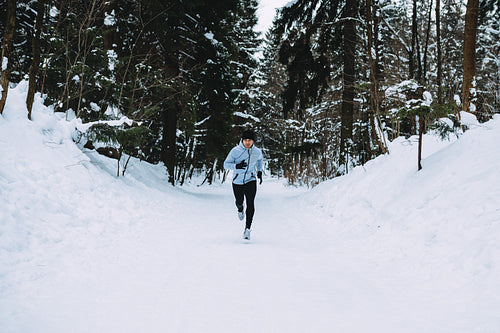 Sportsman running in forest. Young man exercising at winter.