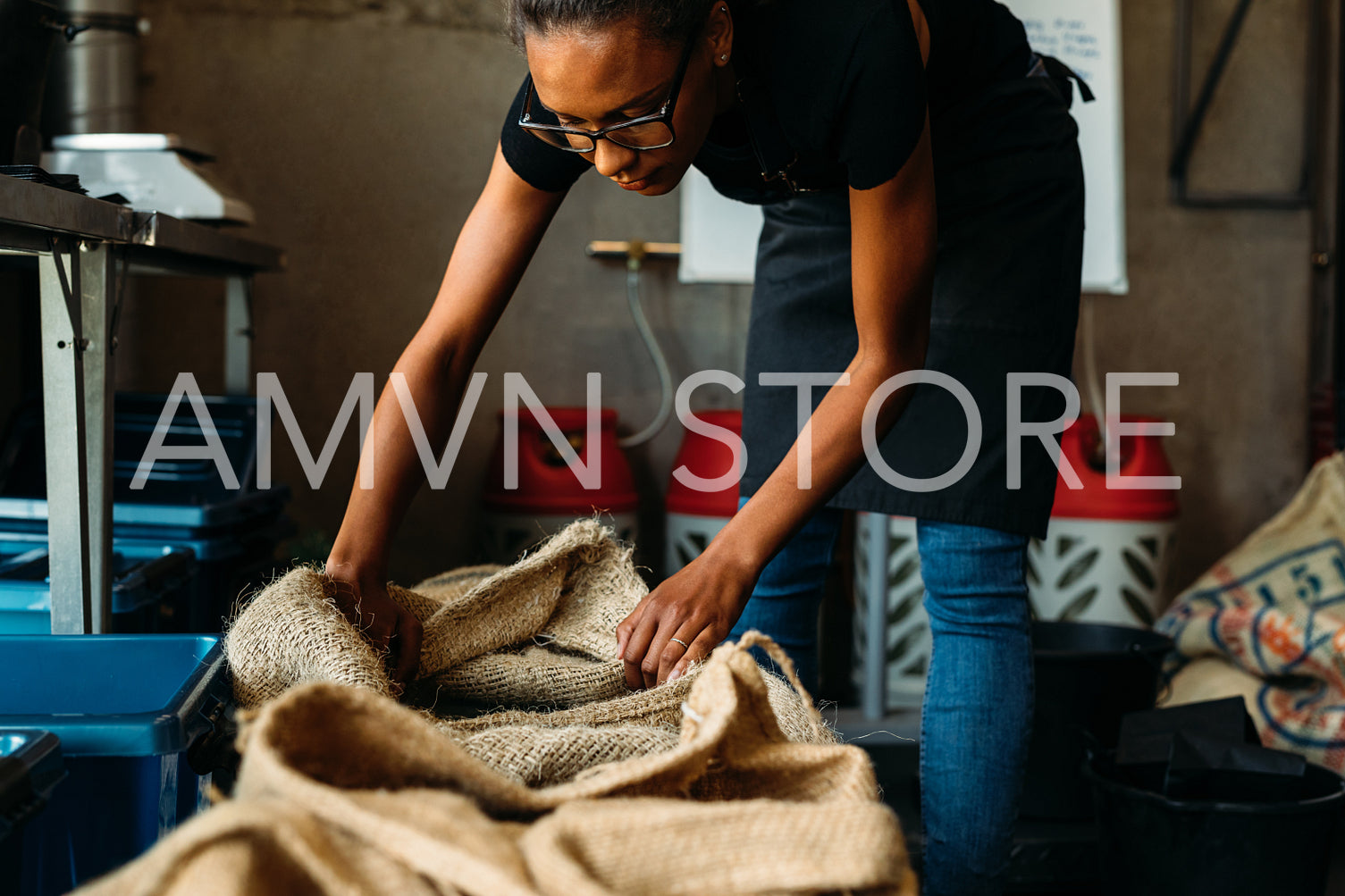 Female entrepreneur standing in storage, looking in a sack with fresh coffee beans