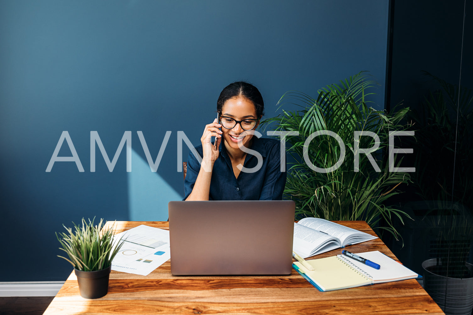 Smiling businesswoman sitting at a table talking on cell phone while working on laptop	