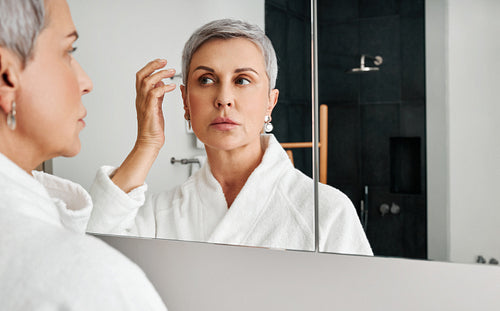 Mature woman adjusting her hairstyle in front of a mirror in bathroom