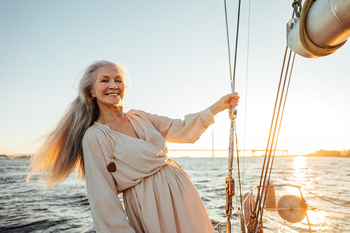 Smiling female wearing dress on private yacht. Senior woman with long white hair looking at camera.