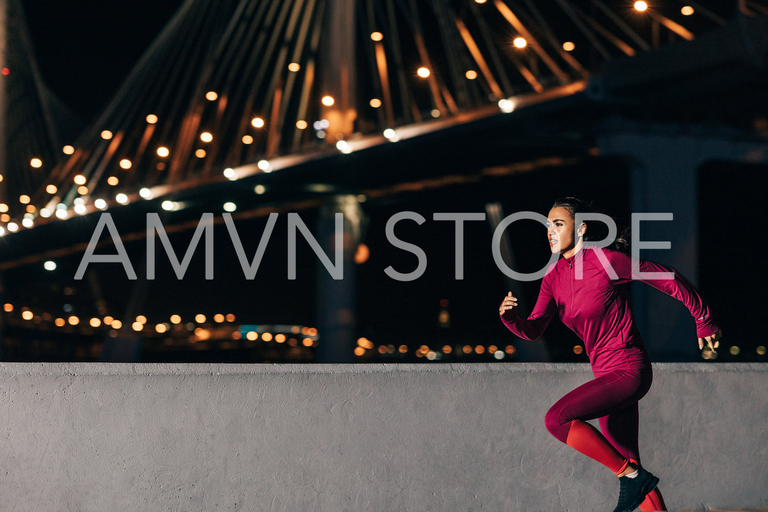 Woman running at night on embankment. Side view of female jogger sprinting outdoors against bridge.