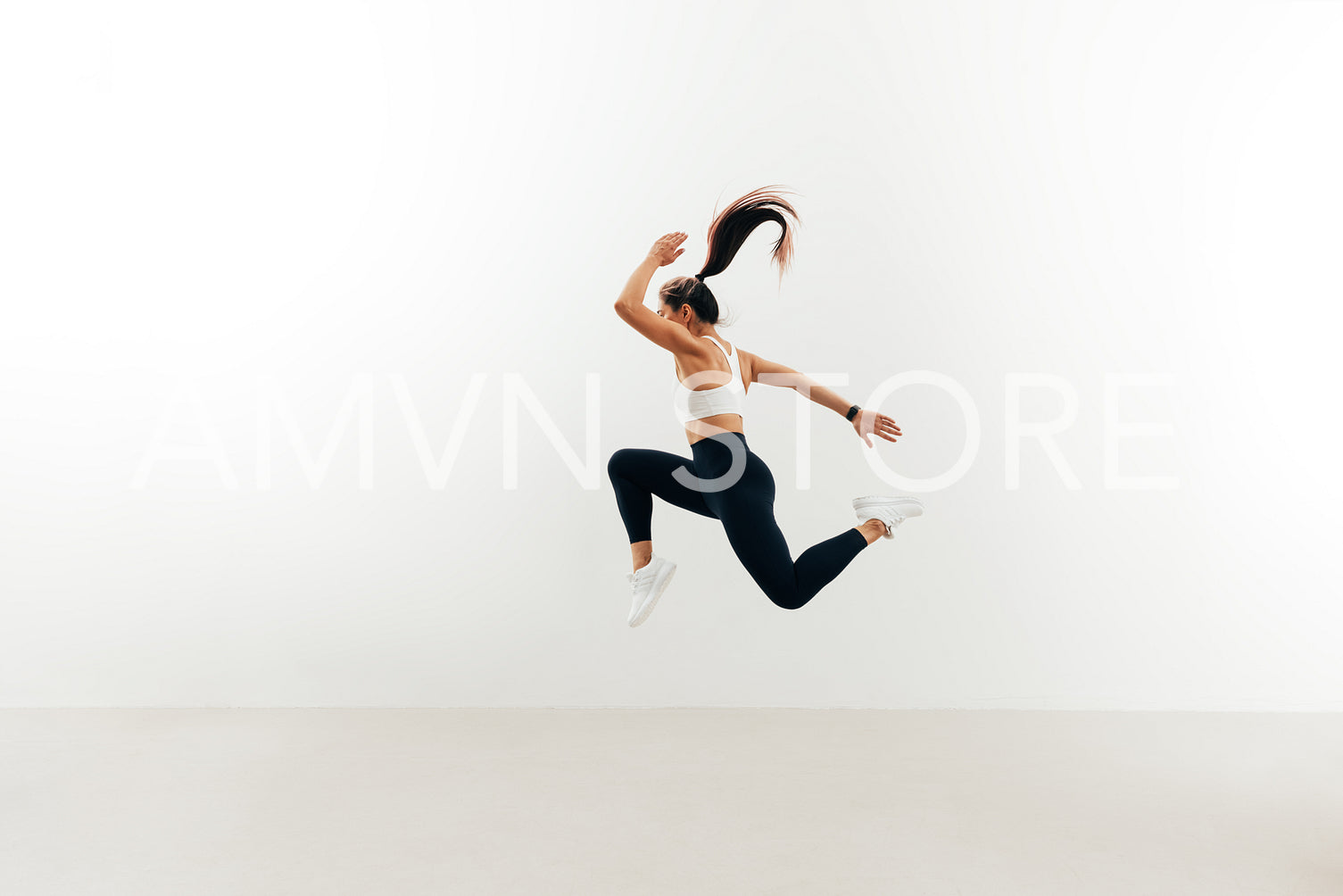 Side view of woman with muscular body jumping against white wall