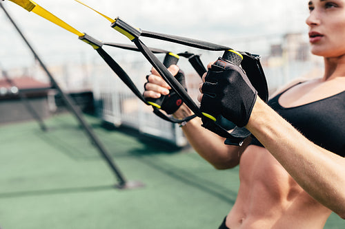 Sporty young woman doing exercises with suspension straps on roof terrace