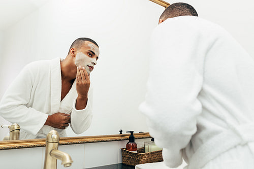 Man looking in the mirror with white clay mask on his face