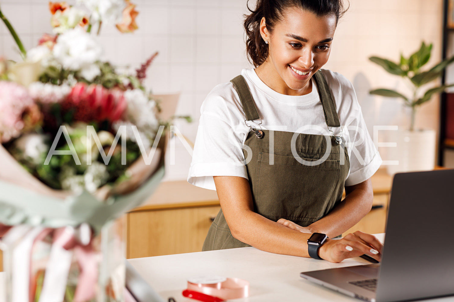 Young flower shop owner using laptop at counter. Woman florist standing at table.	