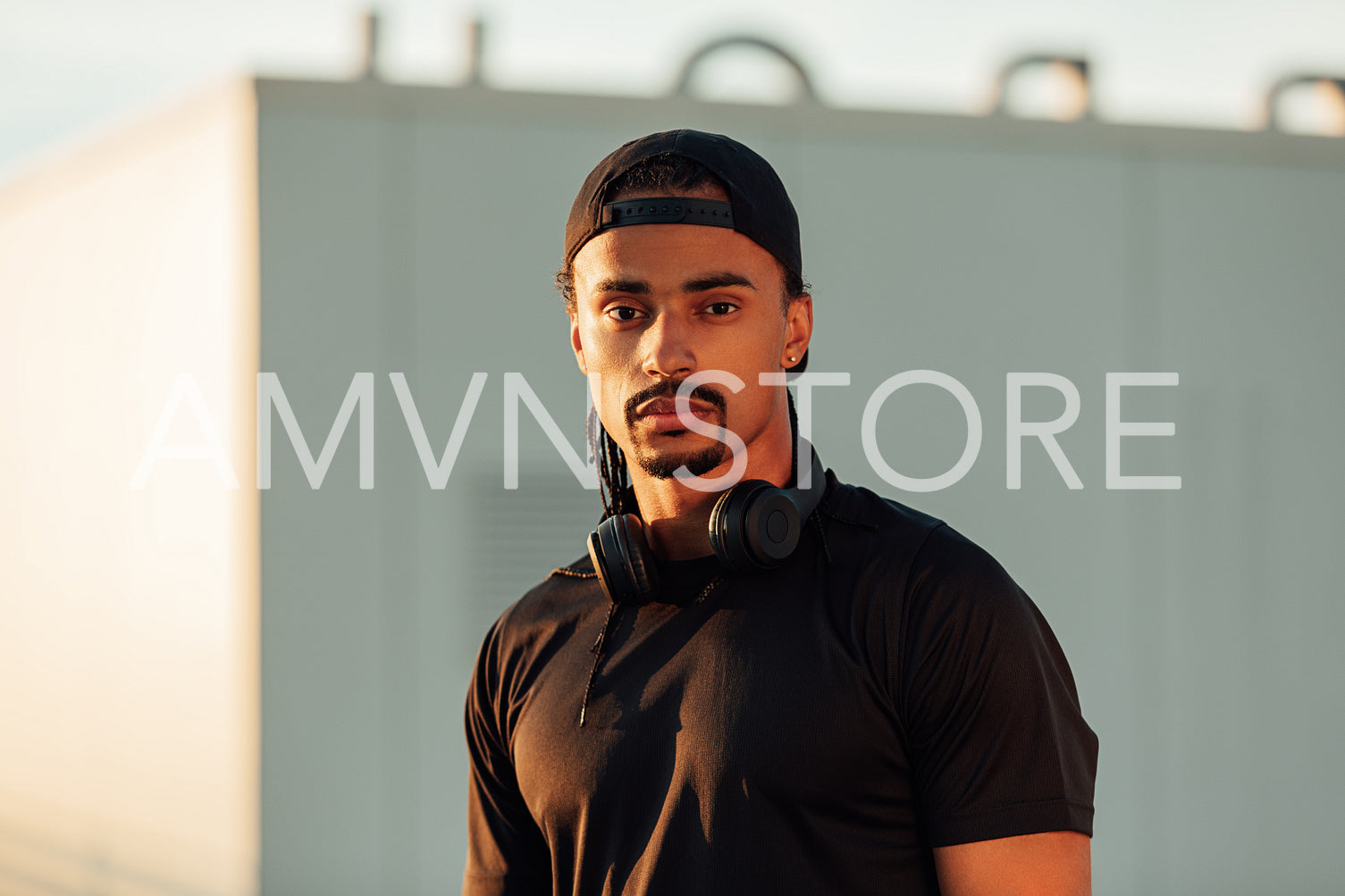 Portrait of a confident male athlete wearing a black cap, wireless headphones, and sports clothes looking at the camera