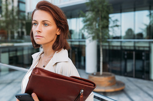 Close up portrait of a middle-aged businesswoman with ginger hair standing outdoors at an office building