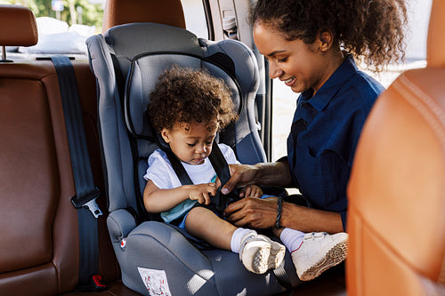 Young woman fastens her son with safety straps in the car