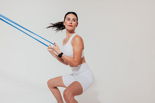 Young woman practicing squats over white background using a resistance band