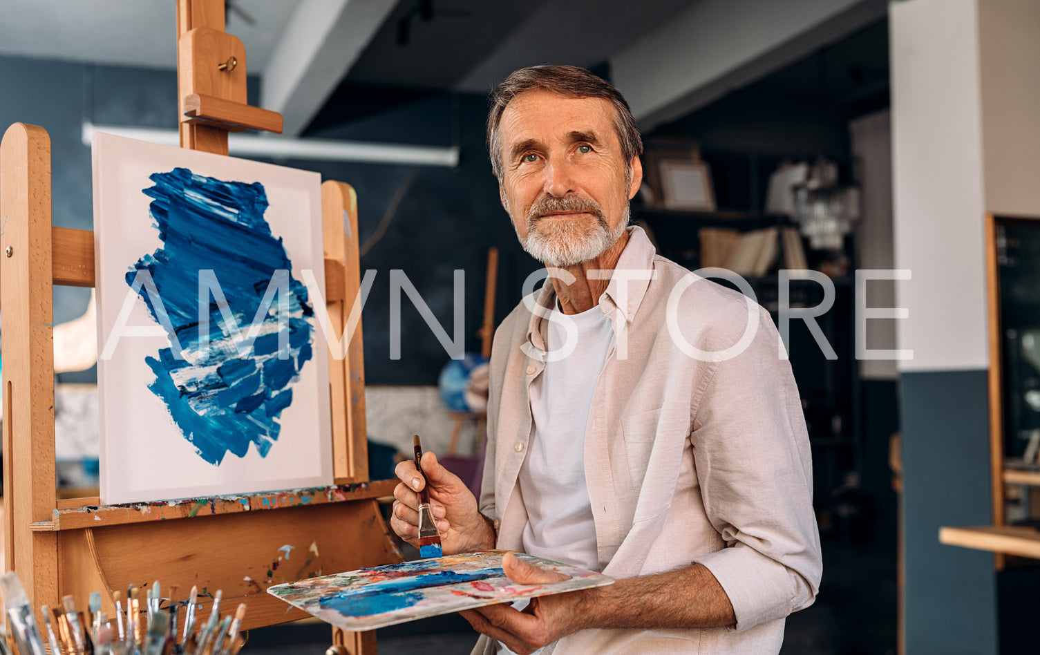 Portrait of a senior painter holding palette with a brush and looking away. Artist in his studio.	