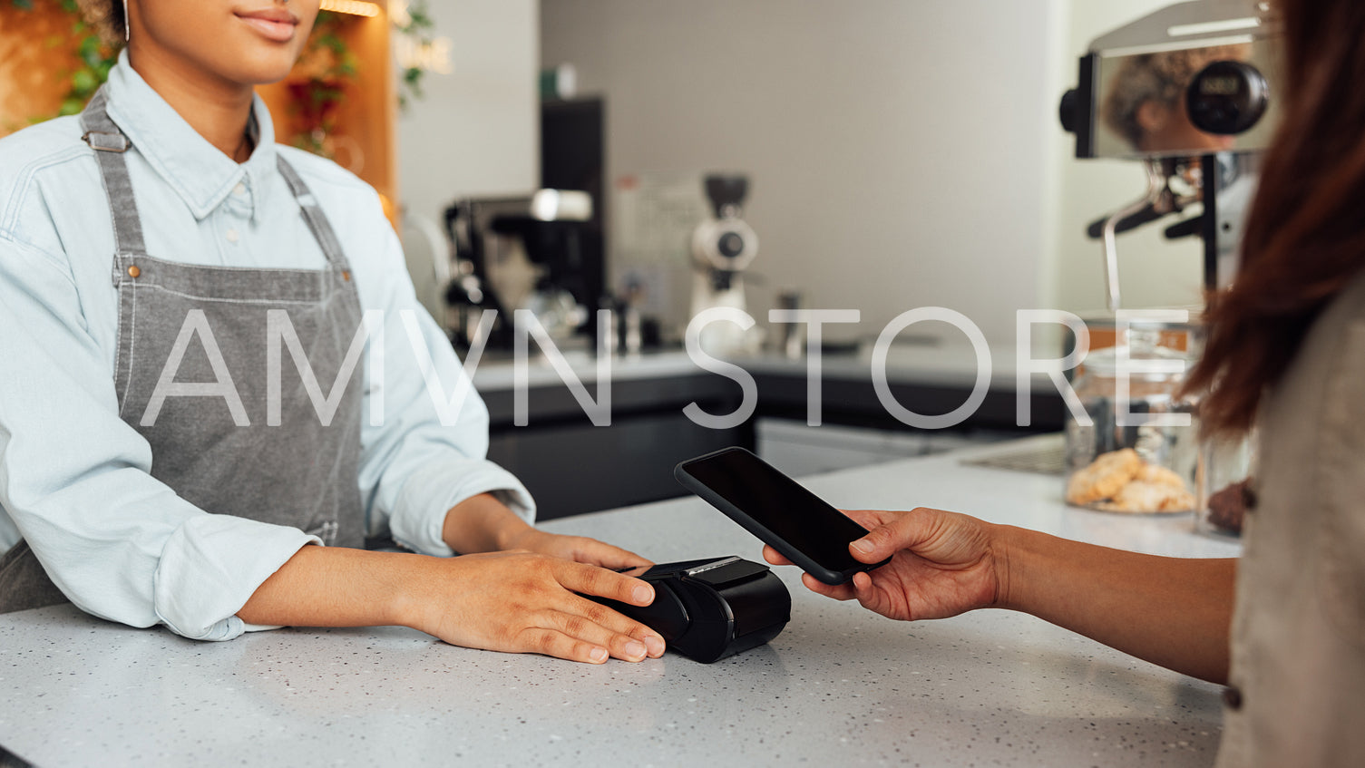 Unrecognizable customer paying by NFC at a cafe. Barista holding pos terminal while receiving payment.