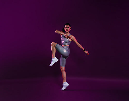 Full length of slim healthy woman warming up over a magenta background, wearing silver fitness attire