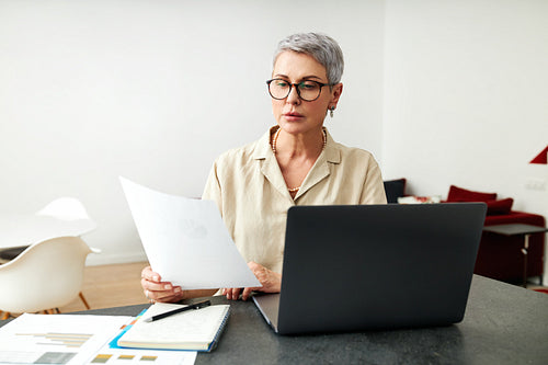 Mature woman with documents using laptop at home